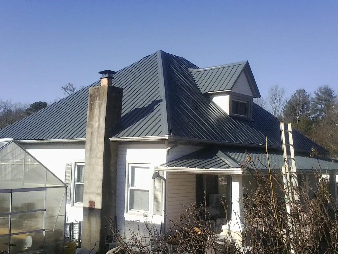 Dark blue standing seam metal roof on a white farmhouse with dormer — Slate & Tile Roof Repair by Roofing Brothers in Windsor Heights