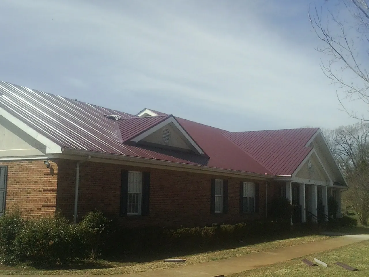 Red metal roof with gabled entries on a long brick building, from a Hail Damage Roof Repair job in Windsor Heights