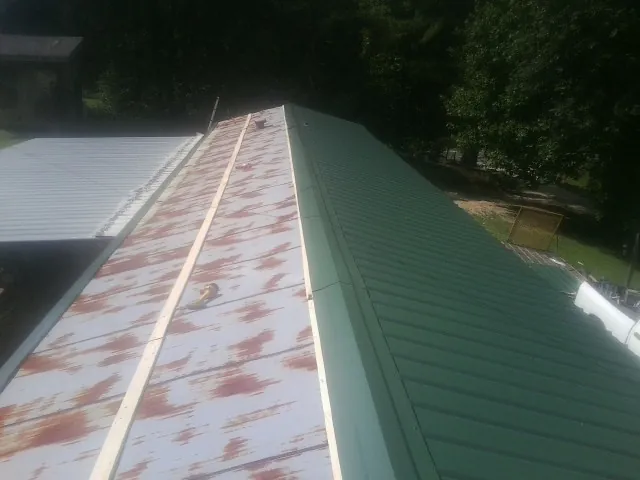Old rusted panels beside newly installed green metal roofing — Wind Damage Roof Repair by Roofing Brothers in Windsor Heights