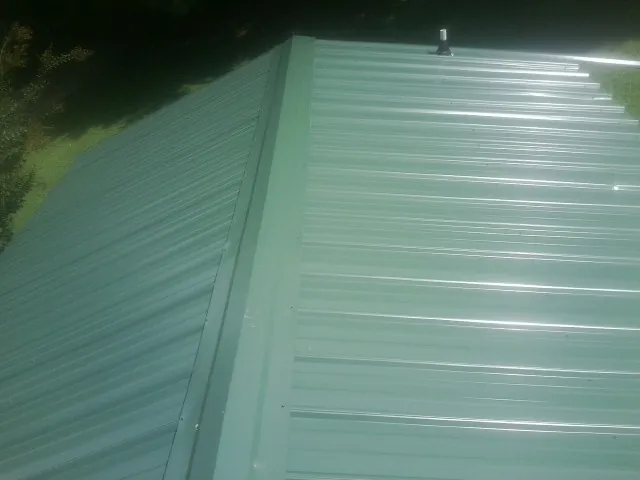 New green metal panels meeting at the ridge of a roof — Flat Roof Repair work by our crew in Windsor Heights