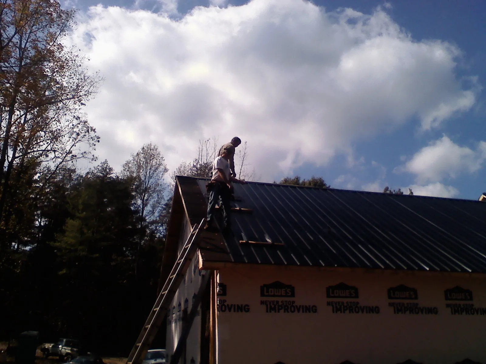 Roofer fastening dark metal panels high against a cloudy sky, from a Roof Inspection job in Windsor Heights