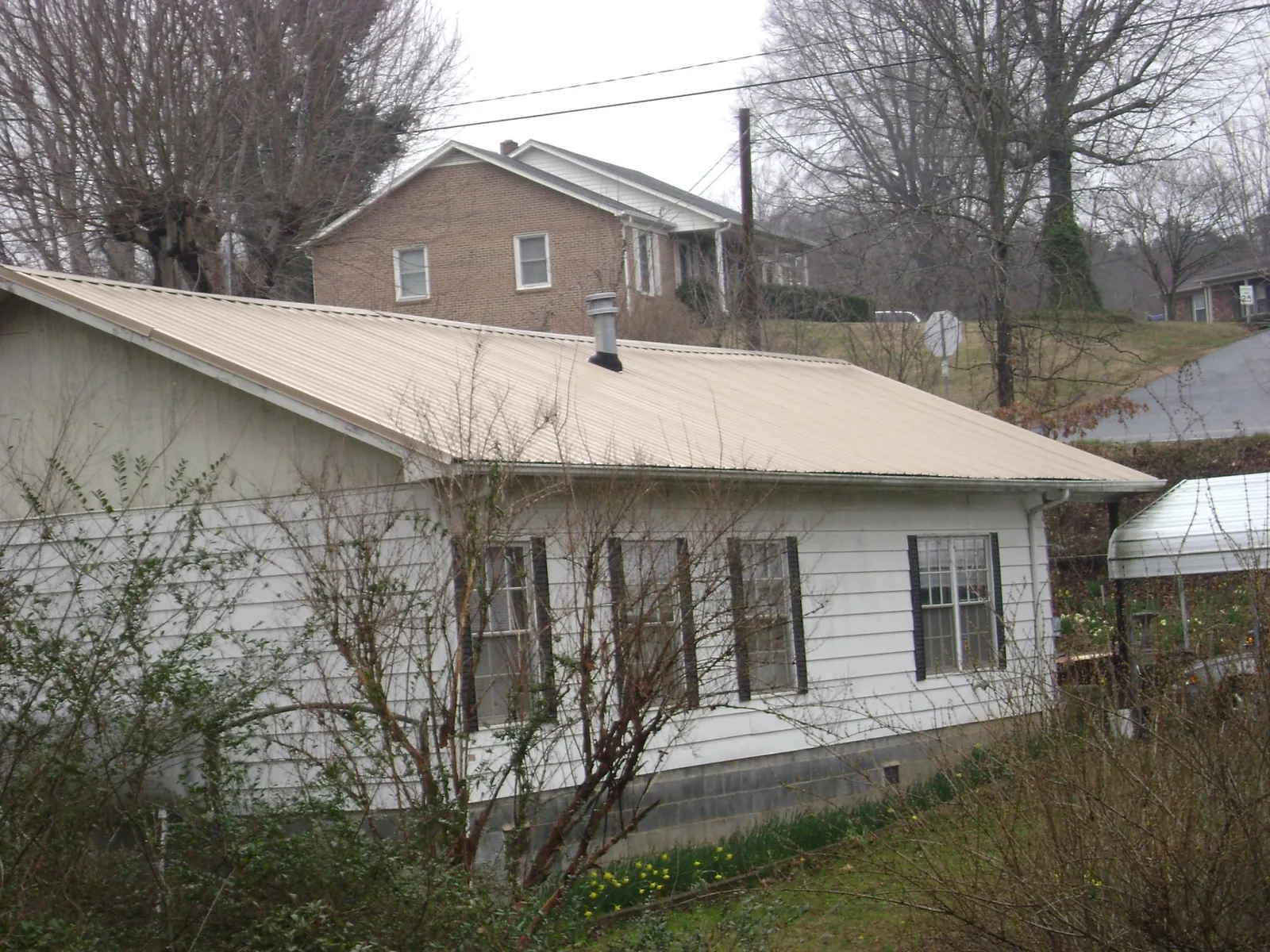 Tan metal roof on a white sided house set into a hillside — Commercial Roofing by Roofing Brothers in Windsor Heights