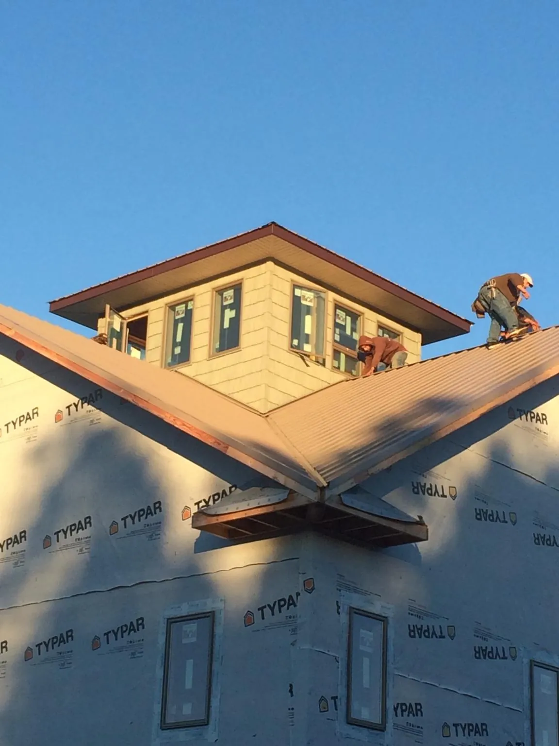 Roofers working around a rooftop cupola on a new metal roof at sunset — Roof Waterproofing in Windsor Heights by Roofing Brothers
